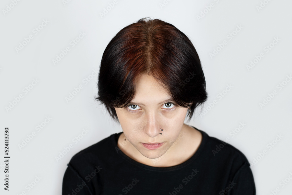 Portrait of a young girl looking from under the forehead, the girl has sad but beautiful face and painted brown hair, the girl has a difficult adolescence, those around her do not understand her Portrait of a young girl looking from under the forehead, the girl has sad but beautiful face and painted brown hair, the girl has a difficult adolescence, those around her do not understand her