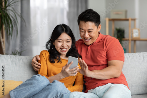 Cheerful chinese spouses using cell phone, home interior