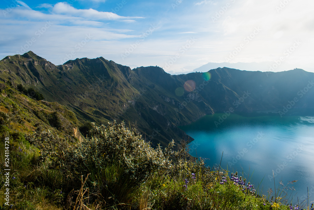Quilotoa crater, one of Ecuador's touristic and hiking destinations during a sunny day with cloudy blue sky. Ecology, mountains and tranquility concept.
