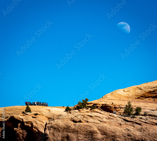 Jeep expedition on a high red rock cliff with moon in background