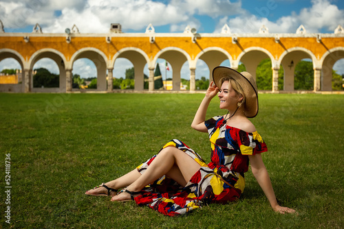 A girl in a hat sits on the grass near the Basilica of San Antonio de Padua. Izamal, Mexico photo
