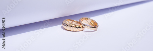 Two gold wedding rings on a white background with contrasting shadows. Banner