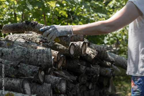 a woman in gloves stacks firewood on a pallet