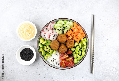 Hawaiian poke with rice, falafel, green edamame beans, avocado, cherry tomatoes and hummus on a gray background, top view.