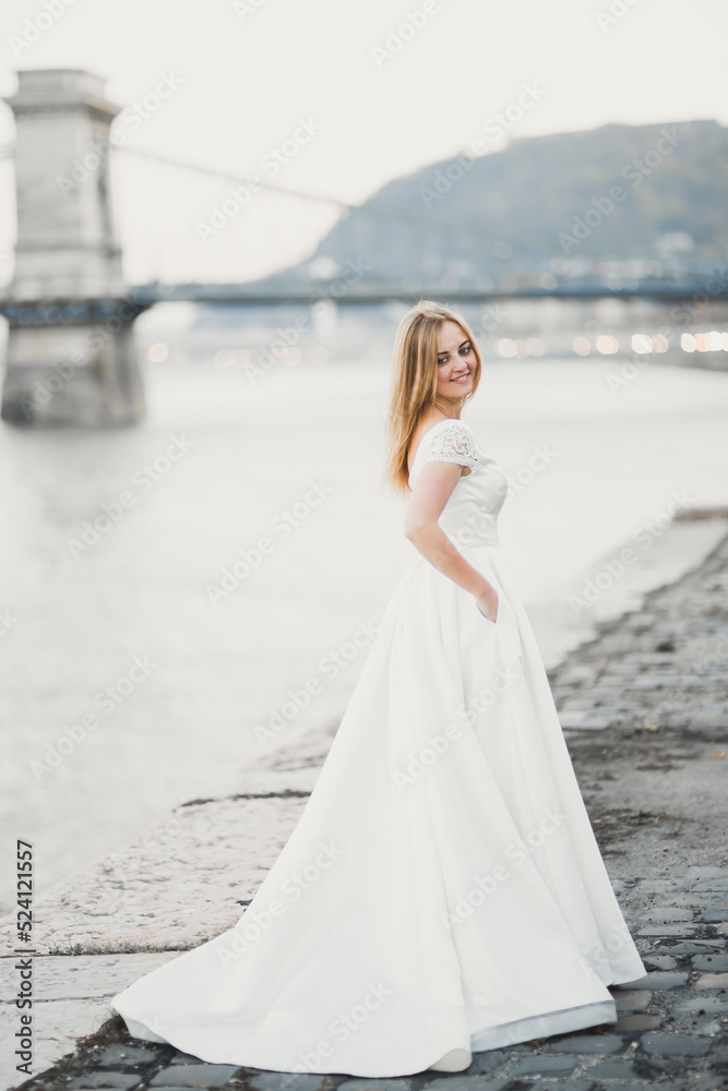 Beautiful brunette bride in elegant white dress holding bouquet posing near river Beautiful brunette bride in elegant white dress holding bouquet posing near river