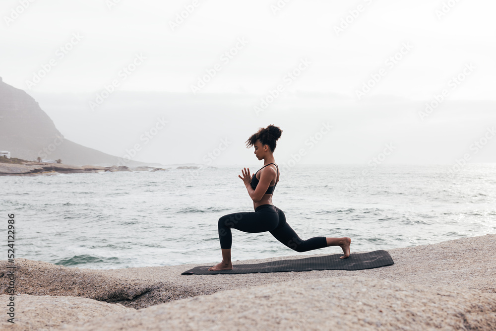 Woman in fitness wear practicing yoga on a mat at seashore