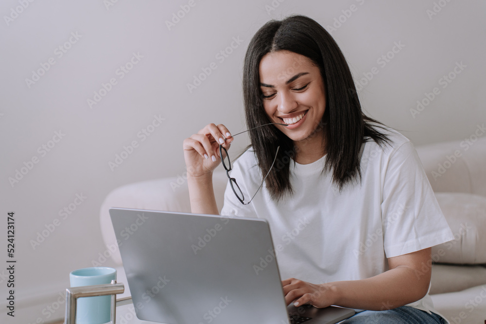 Shy cute African American young woman sitting on sofa with laptop ...