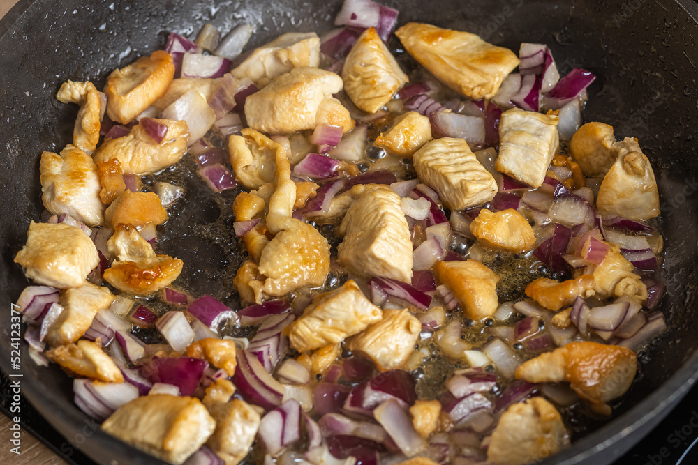 Onions and pieces of chicken breast are fried in a frying pan Onions and pieces of chicken breast are fried in a frying pan