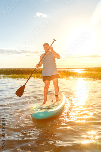 a man on a SUP board with an oar floats on the water against the background of the sunset.