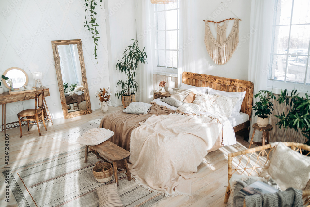 Cozy rustic bedroom with boho ethnic decor. Enter apartment with sun rays  from large windows and wooden furniture. Console table, full-length mirror  and handmade textiles. Plants in pots. Nobody Stock Photo