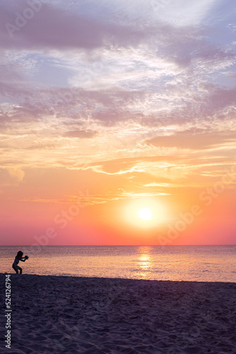 Fototapeta Naklejka Na Ścianę i Meble -  Dark silhouette of a child playing on the beach by sunset. Sea and pastel colours of sky and clouds. Magical sea landscape. Summer vacation.