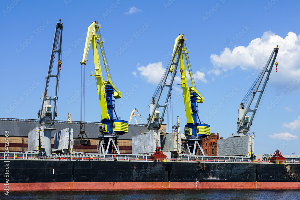 Yellow and blue painted cranes load coal into a bulk carrier in the port