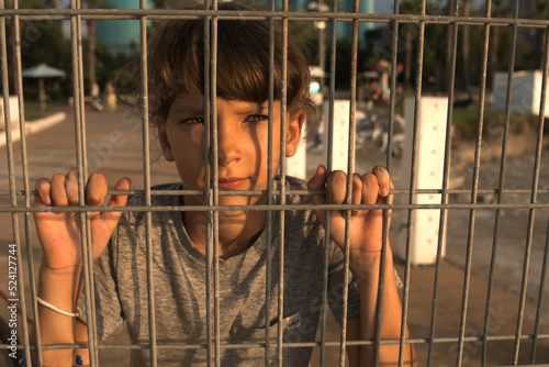 female child looks with a sad face into the distance through an iron grate, close up