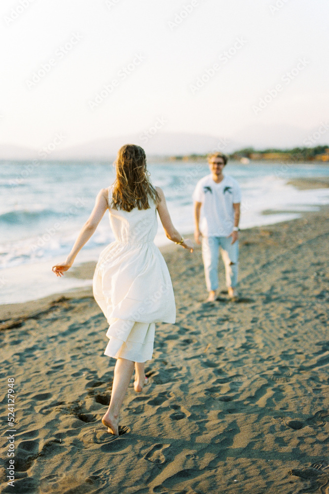 Barefoot girl hurries to man standing on the beach. Back view