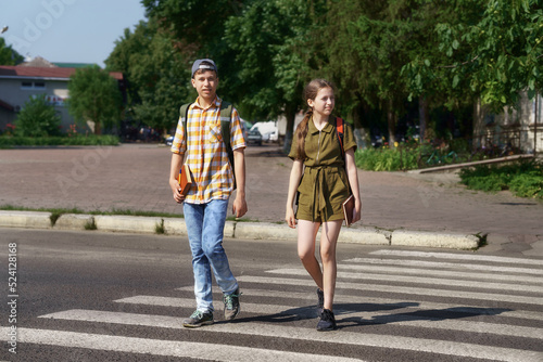 teenage schoolchildren, a boy and a girl cross the road at a pedestrian crossing