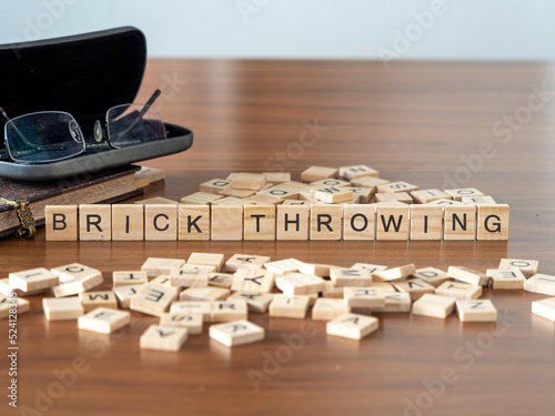 brick throwing word or concept represented by wooden letter tiles on a wooden table with glasses and a book