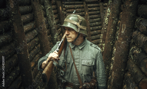 A reenactor of the Finnish army during World War II in a wooden dugout. The uniform of the Finnish army of the past years . A military man with a gun, a photo in vintage processing.
