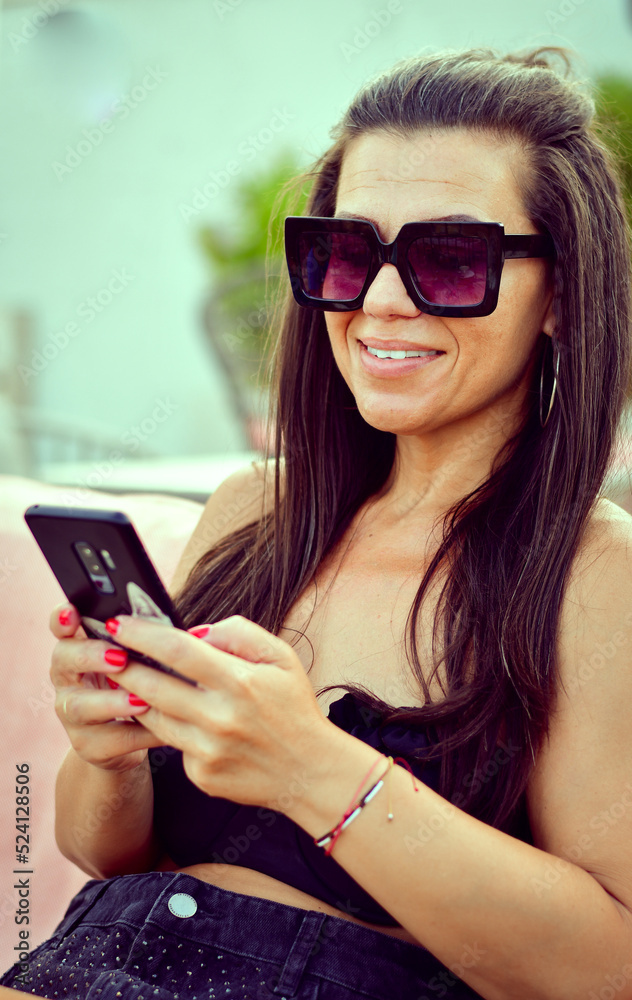 Young Beautiful Happy Smiling Woman in swimsuit looking at the Phone reading a Message ,checking social media and News sitting at beach bar Young Beautiful Happy Smiling Woman in swimsuit looking at the Phone reading a Message ,checking social media and News sitting at beach bar