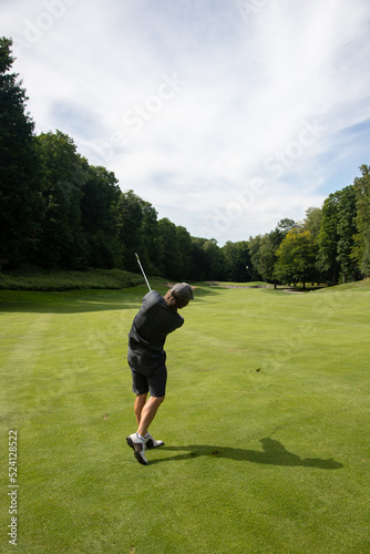 Male golfer in gray, golf swing on fairway surrounded by trees, post-swing