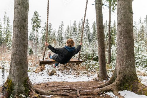 Poland, Rabka-Zdroj  – April 10, 2022: A pregnant woman is swinging outdoors in winter with amazing view on the forest
