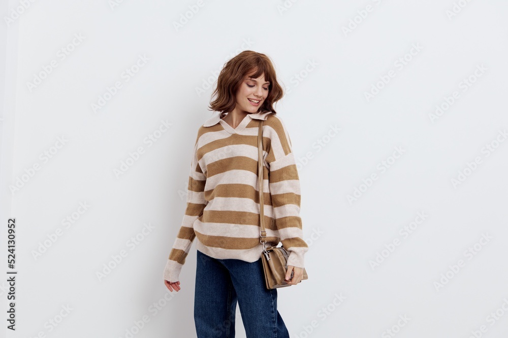 a pretty sweet woman is standing on a light background in a striped sweater and a bag on her shoulder, standing straight with her shoulders slightly twisted a pretty sweet woman is standing on a light background in a striped sweater and a bag on her shoulder, standing straight with her shoulders slightly twisted