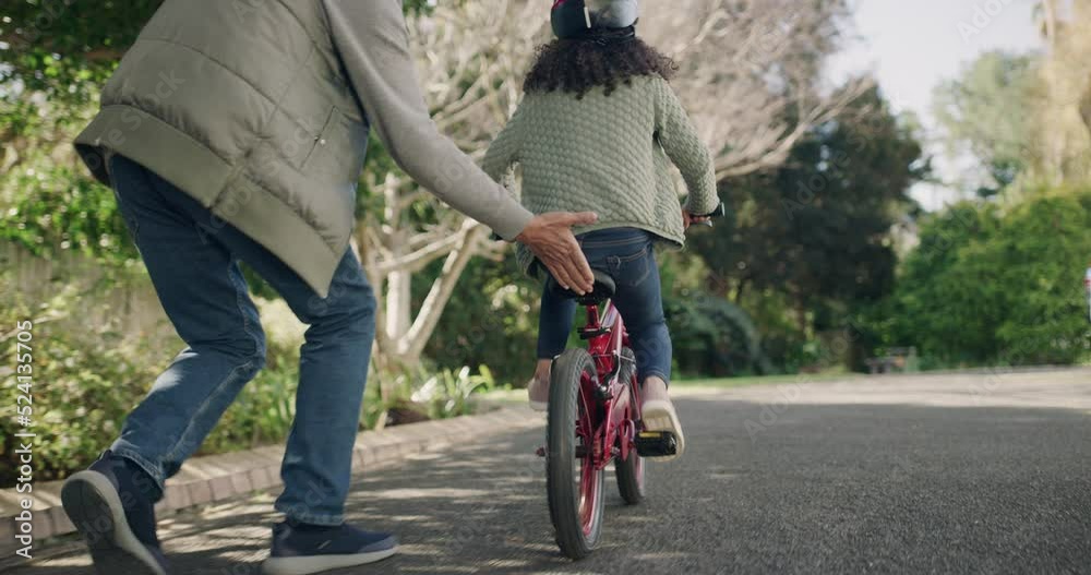 Young girl learning to ride a bicycle in the neighborhood. Loving, caring and proud grandparent helping grandchild to cycle on her own, motivated and determined child cycling in the outdoor nature.