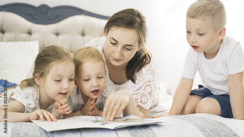 Children lie on the bed in the bedroom, mother reads a book to them. Children lie on the bed in the bedroom, mother reads a book to them.