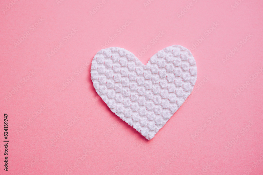 White fabric heart on pink table, top view.
