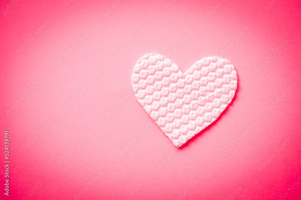 White fabric heart on pink table.