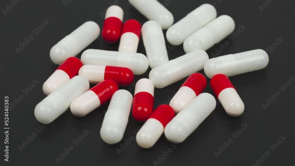 Medical concept. White and red-white capsules lie on the black surface of the rotating table. The table rotates Medical concept. White and red-white capsules lie on the black surface of the rotating table. The table rotates