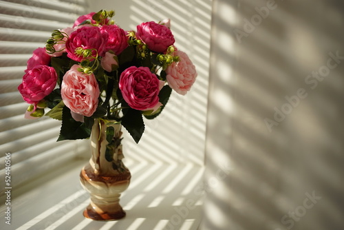 Pink peony flowers in vase on sunny windowsill