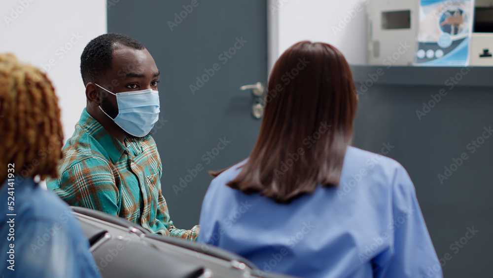 Obraz premium Diverse people talking about disease and coronavirus epidemic, giving advice and healthcare support in waiting area lobby. Nurse and male patient chatting about covid 19 pandemic at facility.