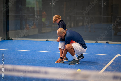 Monitor teaching padel class to child, his student - Trainer teaches little boy how to play padel on indoor tennis court © damianobuffo