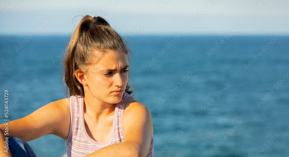young girl in a tank top with a pensive look and the sea in the background with a copy space