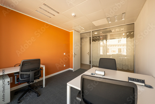 Home office with small white wooden tables, a glass wall, gray carpet and black swivel chairs