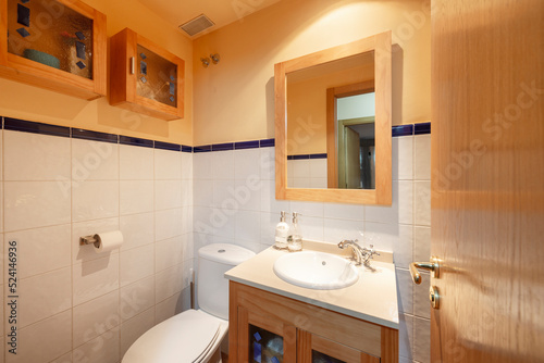 White tile and orange paint bathroom with white porcelain sink  matching wood cabinets  wood framed mirror