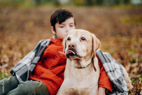 Love to the animals. Raising children to be kind. A boy walks with his labrador retriever in the park in autumn. © sergo321