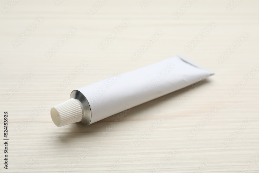 Blank white tube of ointment on light wooden table. Space for text
