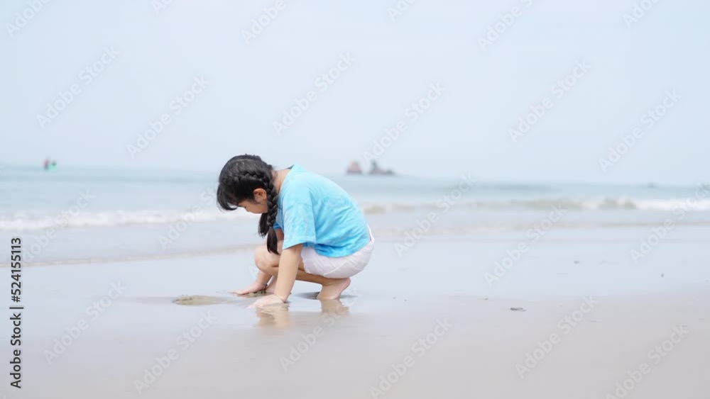Little cute Asian child girl playing sand and sea water on tropical beach in summer sunny day. Happy children kid enjoy and fun outdoor activity lifestyle travel vacation on beach holiday at the sea. Little cute Asian child girl playing sand and sea water on tropical beach in summer sunny day. Happy children kid enjoy and fun outdoor activity lifestyle travel vacation on beach holiday at the sea.