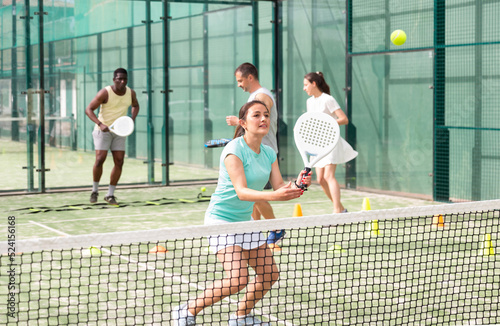 Emotional young adult woman training padel at warm sunny day at group workout © JackF