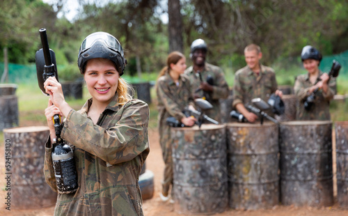 Happy woman and her paintball sport team in protective uniform at shooting range