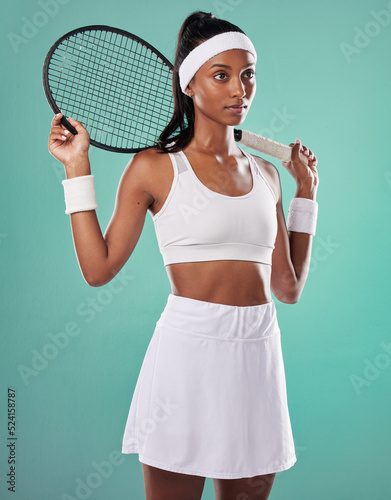 Trendy tennis player, fit athlete and active woman ready to play with racket in cool sports uniform while posing against a green studio background. Competitive, determined and serious young female