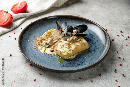 halibut steak on plate with mussels and creamy sauce on grey table photo