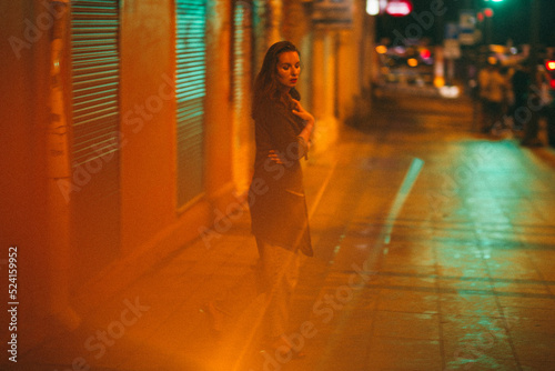 A girl walks around the city at night after the rain among the light of lanterns and cars