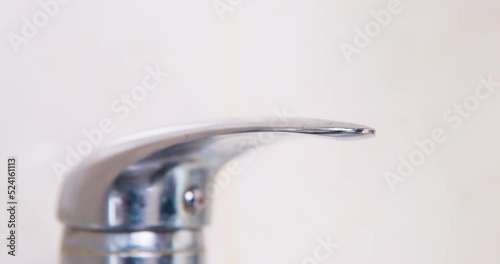 Dog paw presses plumbing chrome faucet, turns off water. Conscious water consumption, cost savings. Conservation of water resources, household ecology. Tap close-up on light background, interior.  photo