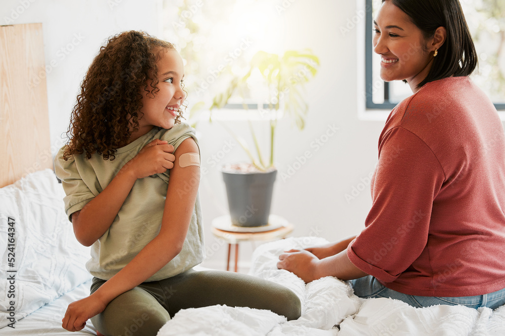 Girl with covid vaccine shows mother vaccinated arm with plaster as covid19 protection for a kid in a bedroom home. Child after getting an injection bonding with her mom in the bedroom - obrazy, fototapety, plakaty 