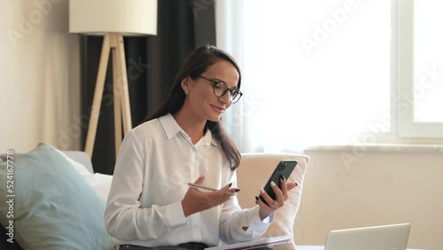 Pretty young woman psychotherapist in white with glasses waves hand beginning online consultation with client at videochat with smartphone in clinic office. People and psychology concept. 4k footage