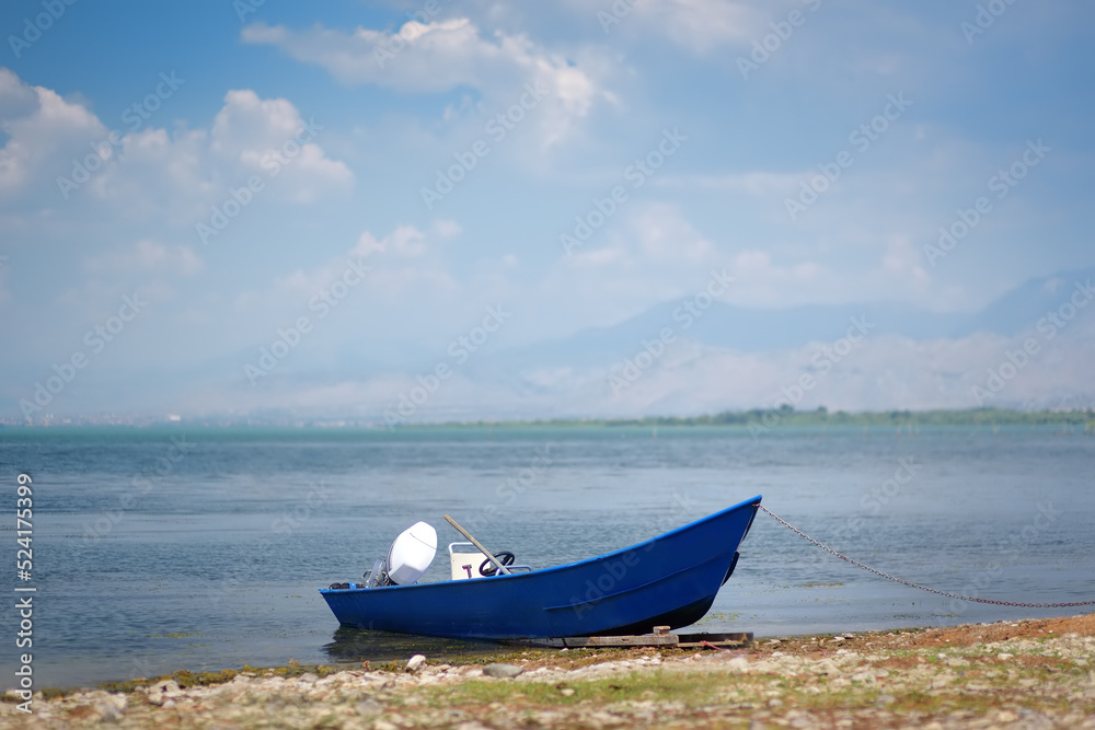 Blue motor boat on shore of wonderful Skadar lake on the background of mountains. Amazing giant Skadar Lake is a famous bird nature reserve in Balkans located in Albania and Montenegro. Blue motor boat on shore of wonderful Skadar lake on the background of mountains. Amazing giant Skadar Lake is a famous bird nature reserve in Balkans located in Albania and Montenegro.