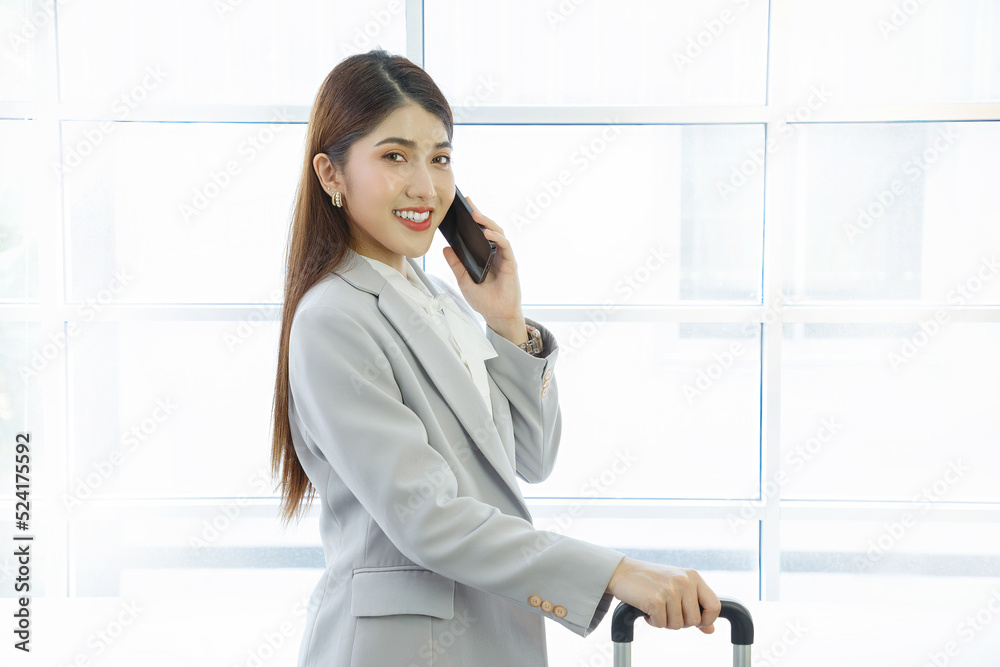 Young businesswoman in a suit pulling a suitcase and talking on the cell phone in front of an airport window Young businesswoman in a suit pulling a suitcase and talking on the cell phone in front of an airport window