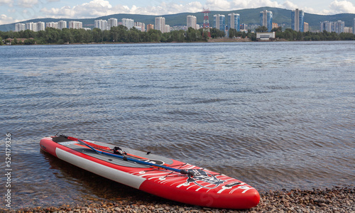 12.07.2022 Krasnoyarsk, Russia. Red SUP board on the river bank. Paddle board on the lake shore. Supboard water tourism and active sports. photo